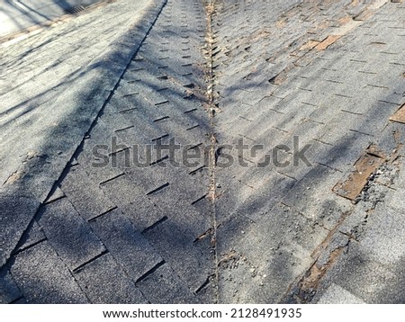 A shot of a rooftop with lots of missing shingles. The roof is severely damaged, weathered, decaying, rotting, and in need of repair or replacement. Royalty-Free Stock Photo #2128491935