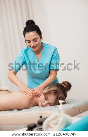 massage therapist does a therapeutic back massage for a woman in the spa