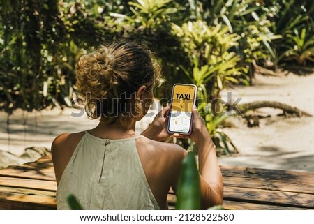 Girl in the park holding a smartphone with Taxi Service app on the screen. Rustic wooden table. Mobility service provider worldwide. Royalty-Free Stock Photo #2128522580