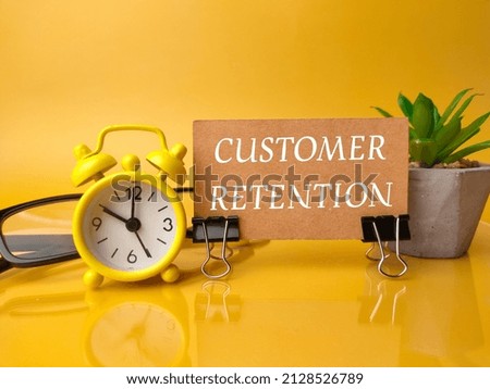 Selective focus.Clock,glasses and green plant with text customer rentention on a yellow background.