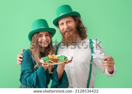 Happy young couple with cookies and paper clover on green background. St. Patrick's Day celebration