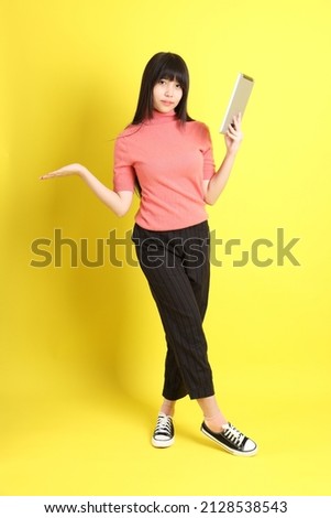 The teen Asian girl with casual dressed standing on the yellow background.