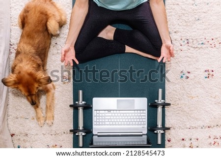 Aerial shot of an unrecognizable woman doing yoga using her computer at home with her dog. Fitness concept.