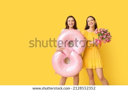 Beautiful women with bouquet of flowers and balloon on yellow background. International Women's Day celebration Royalty-Free Stock Photo #2128552352