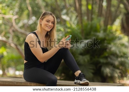 Young woman using a smartphone at day time with a green park in the background. High quality photo. Mobile phone, technology, urban concept. High quality photo
