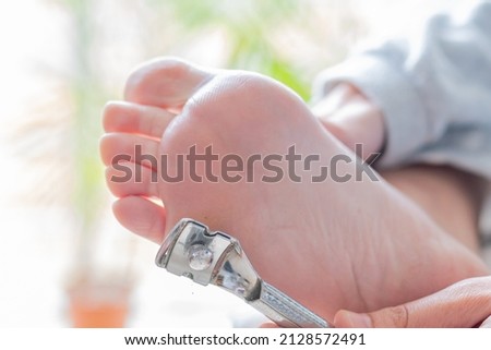 hands of a young woman using a special foot blade to remove calluses.concept body care, pedicure and foot reflexology Royalty-Free Stock Photo #2128572491