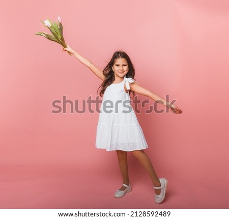 Little cute girl holding a bouquet of tulips on a pink background. Happy women's day. Place for text. Vivid emotions. March 8