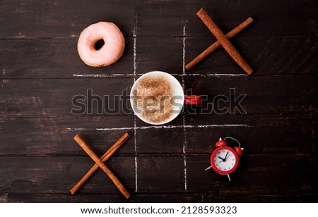 tic tac toe game with donut, clock, cup of coffee and cinnamon sticks on a wooden table