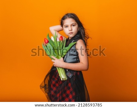Little cute girl holding a bouquet of tulips on a yellow background. Happy women's day. Place for text. Vivid emotions. March 8