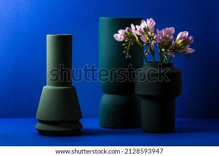 still life on a blue background with green decorative vases and delicate freesia flowers