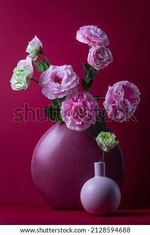 still life on a burgundy background with vases and pink lisianthus