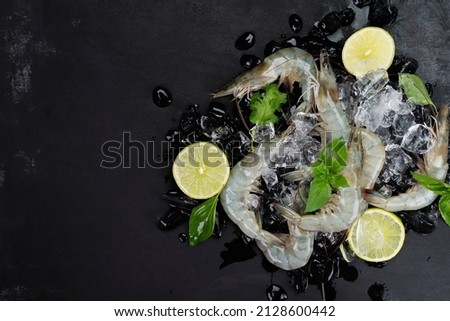 Fresh shrimp with lemon basil leaves on ice Raw shrimp from the sea placed on a black table, seafood menu, top view.