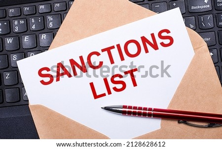 White card with the text SANCTIONS LIST in a craft envelope on a work desk with a modern laptop keyboard and burgundy pen. Flat layout of the workplace.