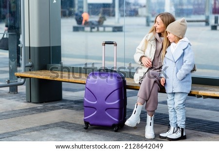 Mom and daughter are sitting at the bus stop and waiting for the bus. Mom shows something to her daughter in the distance Royalty-Free Stock Photo #2128642049