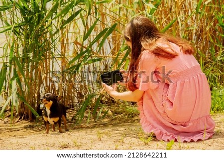 A teenage girl takes a picture of her black Chihuahua dog outdoors. A girl is filming a dog.
