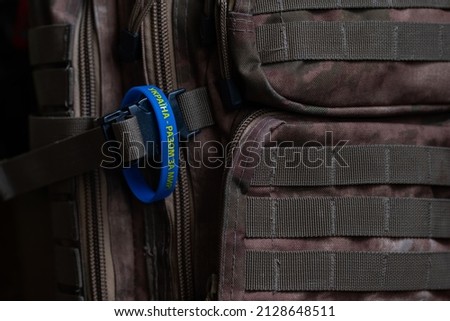 Yellow-blue bracelet with an inscription in Ukrainian: "Ukraine - together for peace!" Prevention of hostilities in Ukraine. Peace concept. Military backpack of khaki color. Camouflage backpack