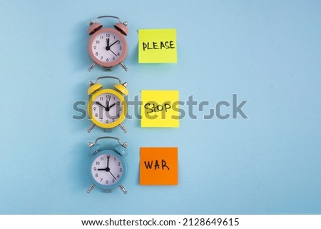 Please stop war. Handwritten inscription on colored notes and multi-colored alarm clocks on a blue background