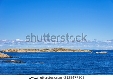 Skerries and coastline under a bright cloudy blue sky in the Koster fjord between the Koster islands and Strömstad, Bohuslän, Västra Götalands län, Sweden. Royalty-Free Stock Photo #2128679303