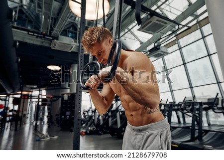 Strong man doing exercise on to gymnastic rings at gym. Fit male athlete training on gymnastic rings in light sport hall