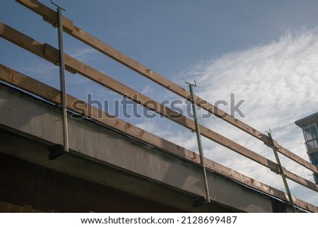 fall arrest scaffolding on a construction site. roof with wooden railings for construction site, on the edge of the roof hooked to the eaves of the roof of the building. Royalty-Free Stock Photo #2128699487