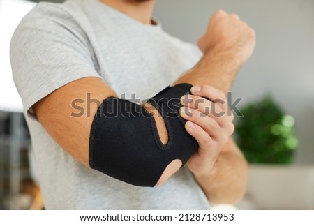 Hand injury. Close up of black elastic supportive medical bandage on elbow of man who is recovering from injury. Man is forced to wear bandage on his arm after broken bone or after sports injury. Royalty-Free Stock Photo #2128713953