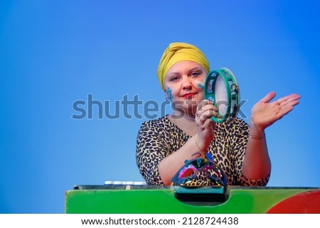 A Jewish woman in a headdress with a painted magen david face controls the noise on Purim while reading a scroll with a tympanum on a blue background. horizontal photo