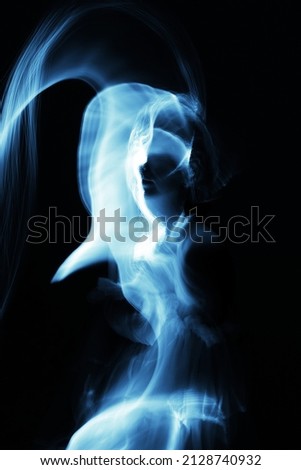 Abstract woman silhouette in light trails of light painting with blue light beams. Portrait in the style of light painting. Long exposure photo. Image contains noise and motion blur
