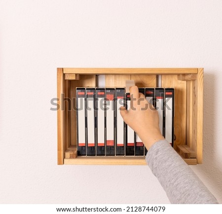 Unrecognizable person picking up a videotape stacked on a shelf on a white wall. Copy space. Concept retro and 90's nostalgia.