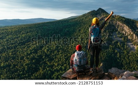 A traveling couple in hiking gear in the mountains at sunset. Two tourists on the top of the mountain. A man and a woman in the mountains. Hiking in the mountains with backpacks. Two travelers Royalty-Free Stock Photo #2128751153