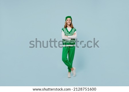 Full size body length excited stunning fun young brunette girl teen student wears checkered green vest hat look camera hold hands crossed isolated on plain pastel light blue background studio portrait