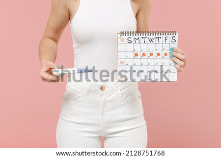 Close up cropped photo shot woman in white clothes hold female periods calendar check menstruation days pregnancy test isolated on pastel pink background. Medical healthcare gynecological concept.