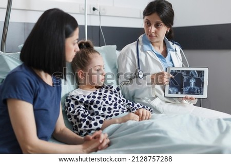 Healthcare pediatric clinic radiology expert talking about x-ray scan results of ill little girl. Hospital radiologist analyzing radiography scan image results and talking with mother about recovery. Royalty-Free Stock Photo #2128757288