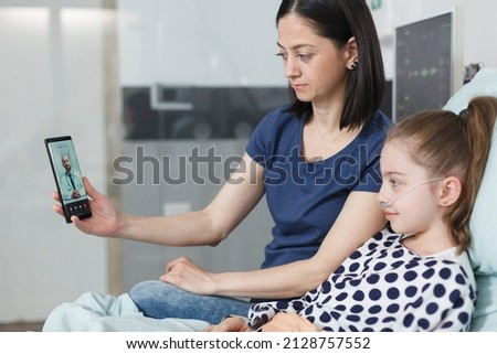 Young mother and sick little child talking with pediatrician on smartphone videocall. Woman and ill girl talking with general practitioner on teleconference while using phone conference app.