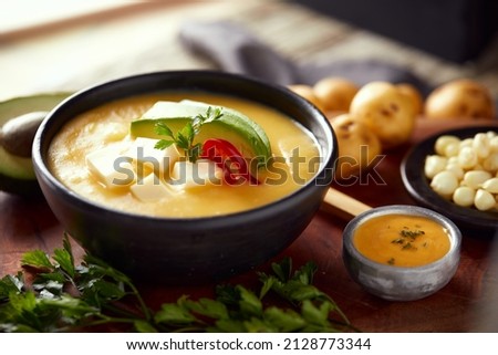 Ecuadorian locro de papa a traditional potato and cheese soup served with avocado and hominy. It’s on a wooden background Royalty-Free Stock Photo #2128773344