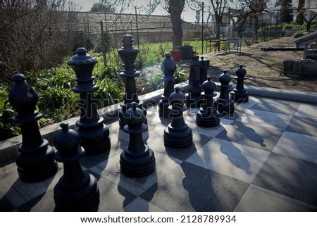 A large outdoor chess set. Here you can see the placement of the black game pieces in the backlight with long shadows. Symbolic image of military strength and an imminent attack