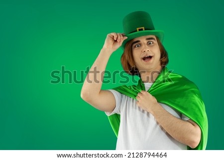 Young man celebranting St. Patrick's Day. Portrait of guy Prep Student with long hair wearing green Leprechaun hat and green cape.