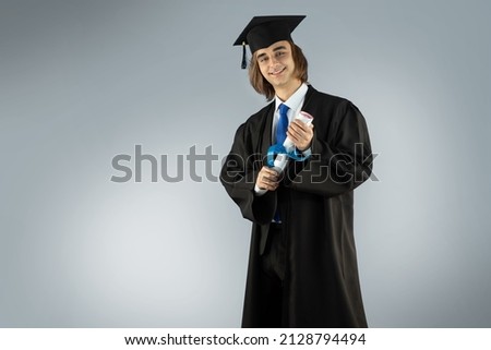 Young man Fresh graduate wearing Graduation robe, Caps with tassel, Gowns, academic dress traditional uniform, formal suit, and tie. Portrait of guy holding blue ribbon diploma, certificate. Royalty-Free Stock Photo #2128794494