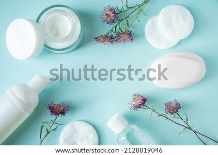 Cosmetic products and dry flowers on blue background. Cream, lotion, soap, and cotton pads. Natural herbal cosmetics. Skin care, wellness concept. Copy space.