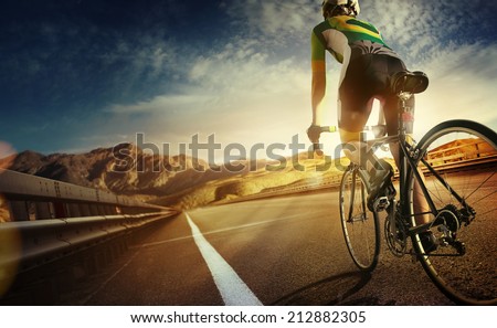 Cyclist riding a bike on an open road to the sunset  Royalty-Free Stock Photo #212882305