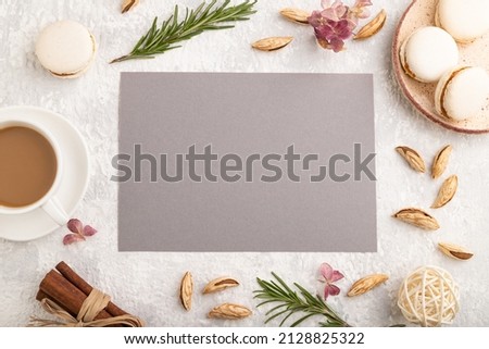 Gray paper sheet mockup with cup of coffee, almonds and macaroons on gray concrete background. Blank, business card, top view, flat lay, still life.