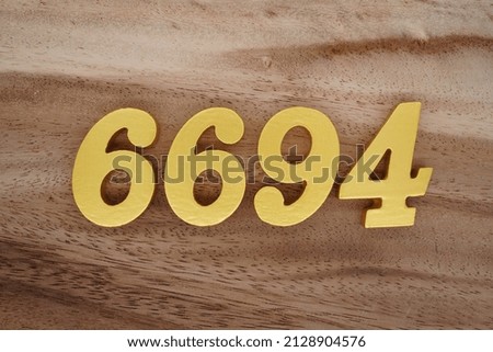 Wooden  numerals 6694 painted in gold on a dark brown and white patterned plank background.