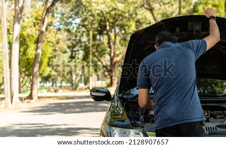 Man stands and inspects a broken-down car in a rural suburban forest. Black car, Engine won't start. Concept for roadside, damaged, stress, fix, problem. Close up, Selective focus, blurred background Royalty-Free Stock Photo #2128907657