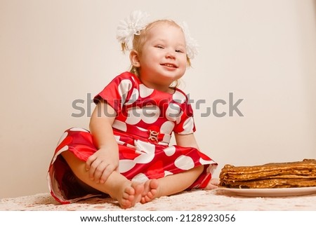 cheerful little girl sits on a table and tastes festive pancakes. shrovetide