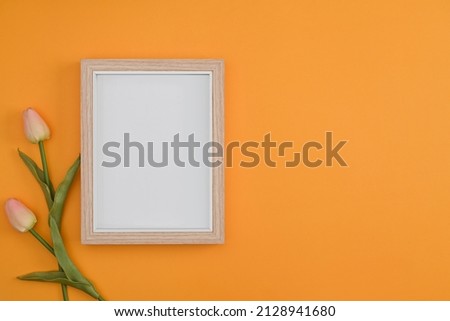 Empty wooden picture frame and pink tulips on yellow background.