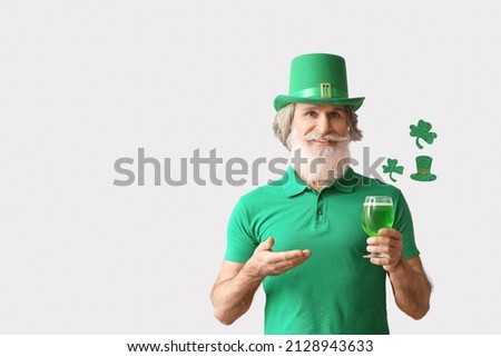 Senior man in green hat with beer on light background. St. Patrick's Day celebration