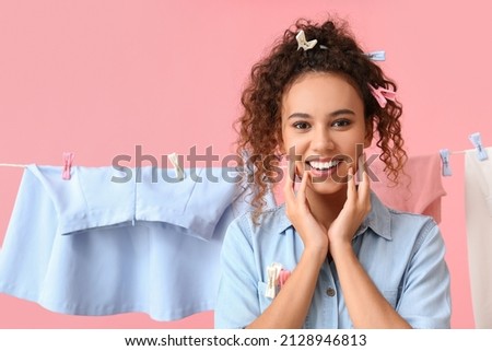 Young African-American woman with hanging laundry and plastic clothespins on pink background