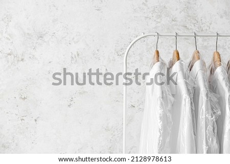 Rack with clean white shirts in plastic bags on grunge background Royalty-Free Stock Photo #2128978613