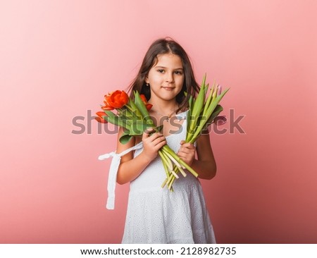 Little cute girl holding a bouquet of tulips on a pink background. Happy women's day. Place for text. Vivid emotions. March 8