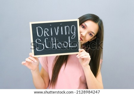 Driving school idea and concept, student driver passed the exam, drivers license, beautiful happy young woman, holding car in her hand. on a gray background. plate with the inscription Driving school