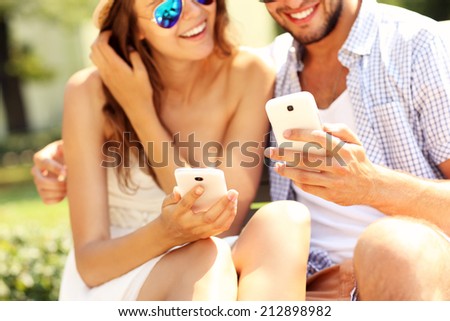 A picture of a young happy couple using smartphones in the park
